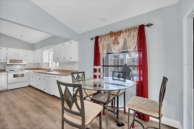 kitchen with tasteful backsplash, white cabinetry, lofted ceiling, light hardwood / wood-style floors, and white appliances