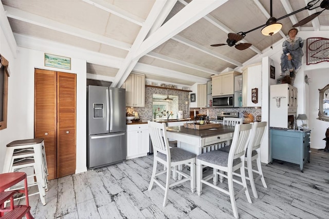 kitchen with vaulted ceiling with beams, appliances with stainless steel finishes, light hardwood / wood-style floors, and backsplash