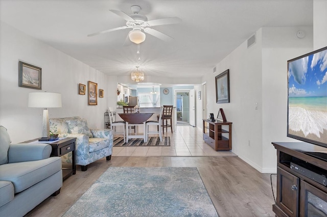 living room with ceiling fan with notable chandelier and light hardwood / wood-style flooring