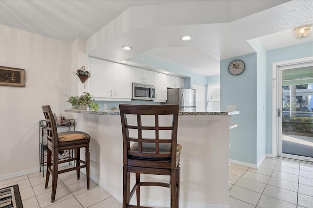 kitchen with light stone countertops, appliances with stainless steel finishes, white cabinets, and kitchen peninsula