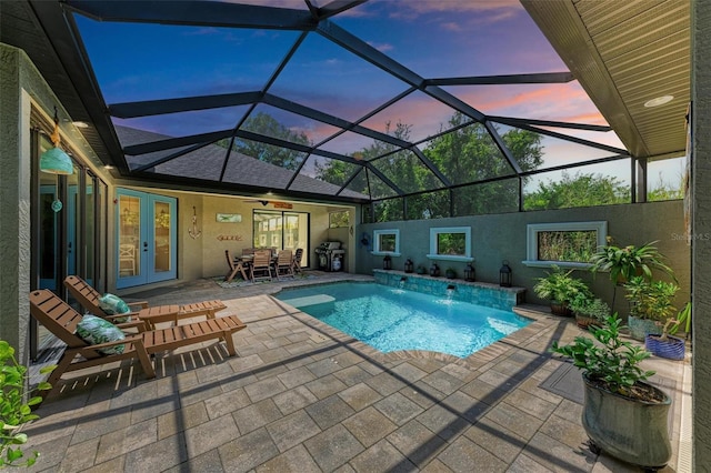 pool at dusk featuring french doors, pool water feature, area for grilling, a lanai, and a patio