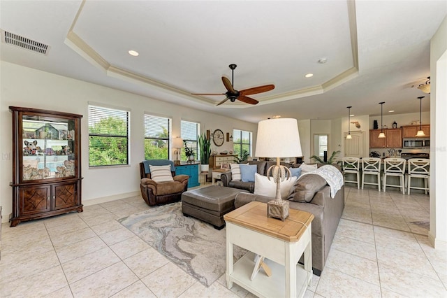 living room with crown molding, a tray ceiling, and light tile patterned floors