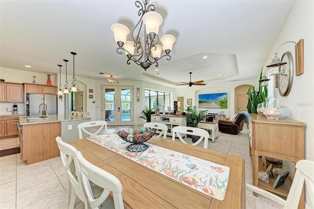 dining area with french doors, sink, light tile patterned floors, a tray ceiling, and ceiling fan with notable chandelier