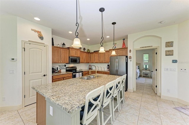 kitchen with decorative light fixtures, a kitchen bar, a kitchen island with sink, light tile patterned floors, and stainless steel appliances