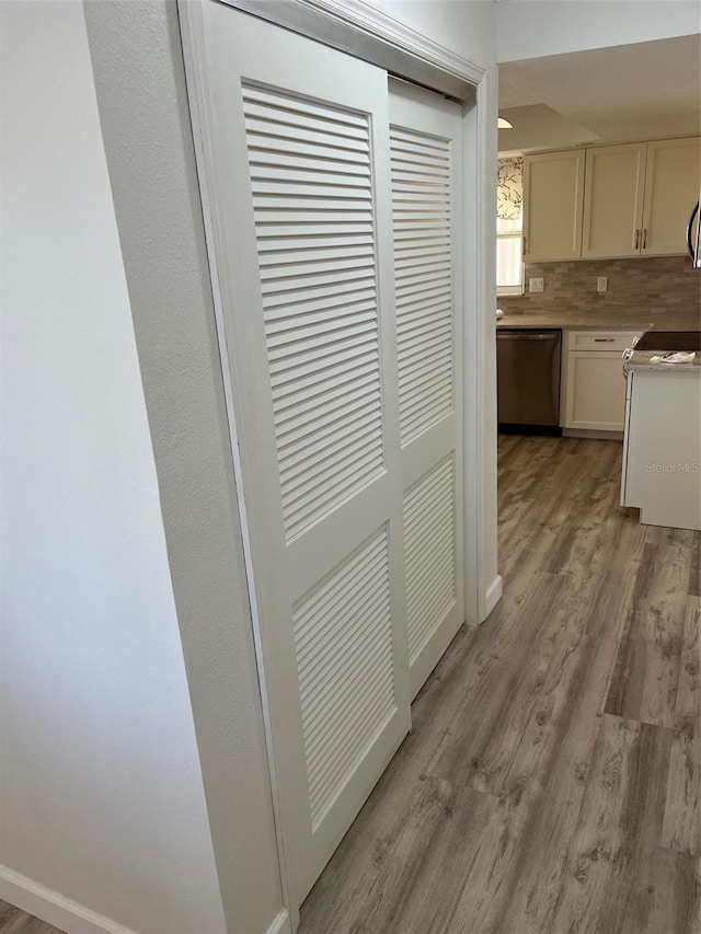 kitchen featuring light countertops, light wood-style flooring, decorative backsplash, stainless steel dishwasher, and baseboards