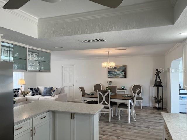 kitchen with light wood-type flooring, visible vents, crown molding, and hanging light fixtures