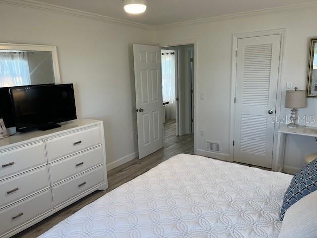 bedroom with baseboards, visible vents, ornamental molding, wood finished floors, and a closet