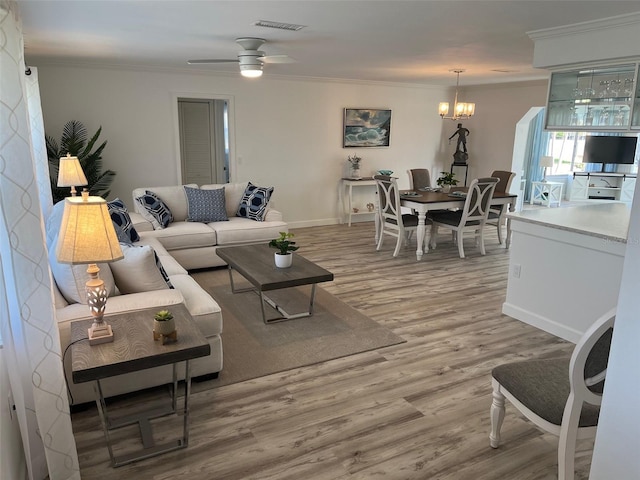 living room with ceiling fan with notable chandelier, visible vents, baseboards, light wood finished floors, and crown molding