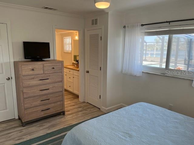 bedroom with light wood-style flooring, ensuite bath, visible vents, and crown molding