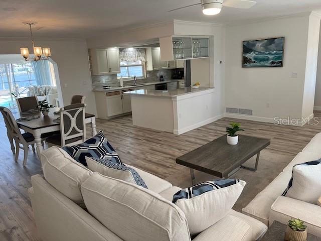 living area featuring a wealth of natural light, visible vents, light wood-type flooring, and ornamental molding