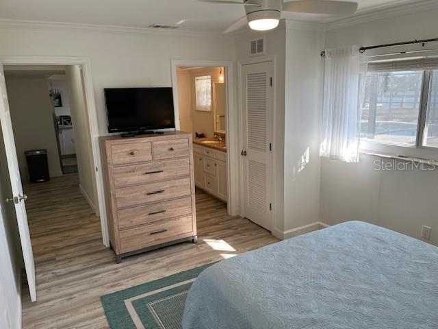 bedroom featuring visible vents, connected bathroom, baseboards, light wood-type flooring, and ornamental molding