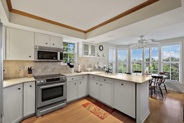 kitchen with sink, stainless steel appliances, ornamental molding, white cabinets, and kitchen peninsula