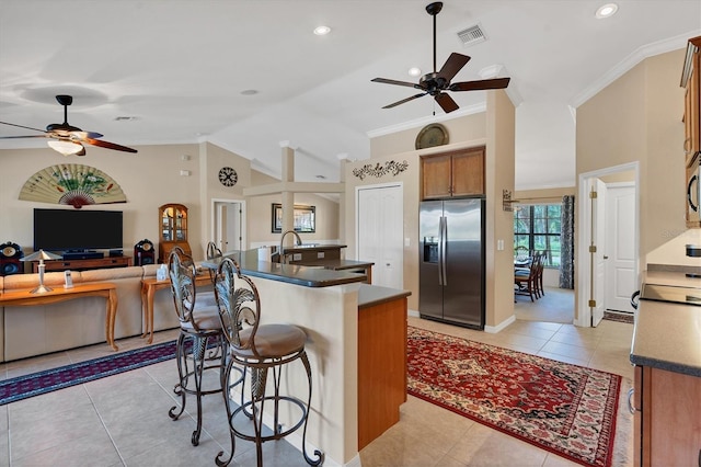 kitchen featuring vaulted ceiling, ornamental molding, a kitchen island with sink, light tile patterned floors, and stainless steel fridge with ice dispenser