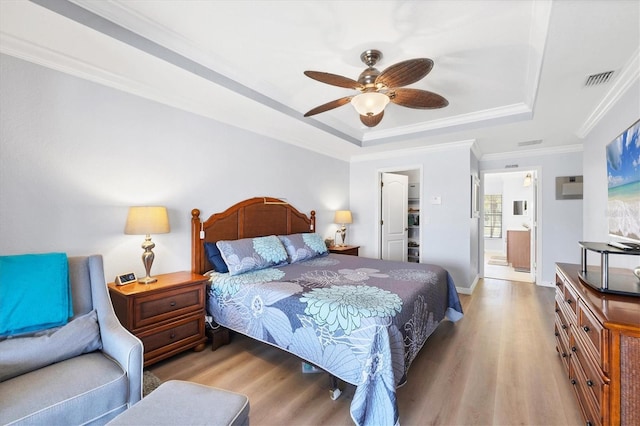 bedroom featuring crown molding, ensuite bath, hardwood / wood-style flooring, ceiling fan, and a tray ceiling