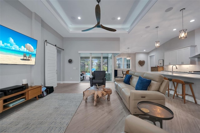 living room with a towering ceiling, ceiling fan, a barn door, and light wood-type flooring