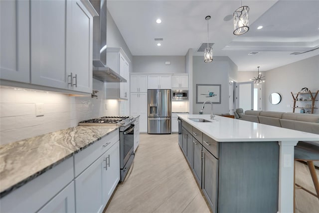 kitchen featuring sink, appliances with stainless steel finishes, pendant lighting, a kitchen island with sink, and wall chimney range hood