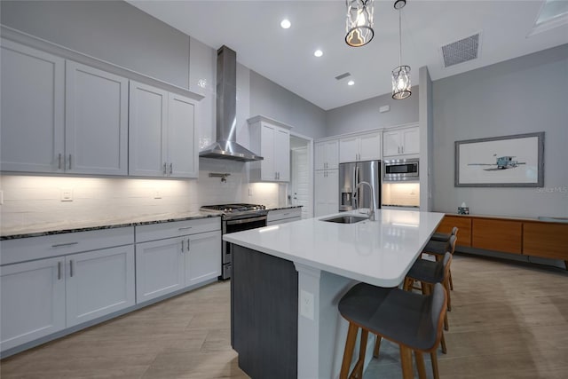 kitchen featuring sink, white cabinetry, hanging light fixtures, appliances with stainless steel finishes, and wall chimney range hood