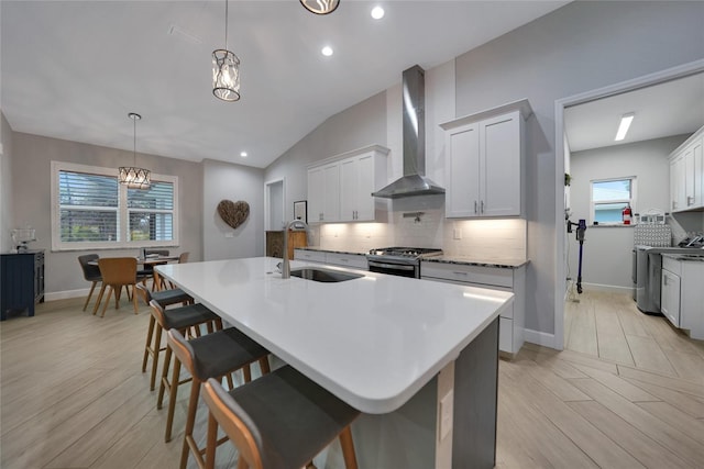 kitchen featuring wall chimney exhaust hood, stainless steel range with gas cooktop, sink, and white cabinets