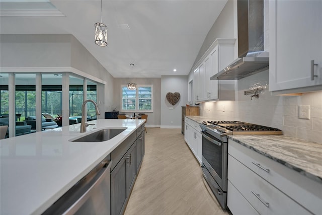 kitchen with sink, decorative light fixtures, appliances with stainless steel finishes, wall chimney range hood, and white cabinets