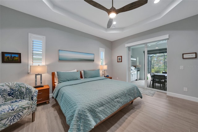 bedroom featuring multiple windows, access to exterior, light hardwood / wood-style flooring, and a raised ceiling