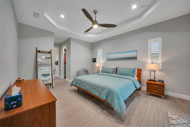 bedroom with multiple windows, light hardwood / wood-style floors, and a tray ceiling