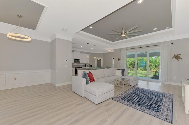 living room featuring crown molding, ceiling fan, a raised ceiling, and light hardwood / wood-style flooring