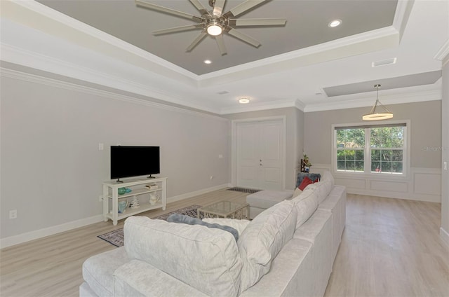 living room with a raised ceiling, ornamental molding, and light wood-type flooring