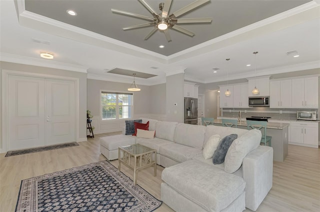 living room with ornamental molding, a tray ceiling, and light wood-type flooring