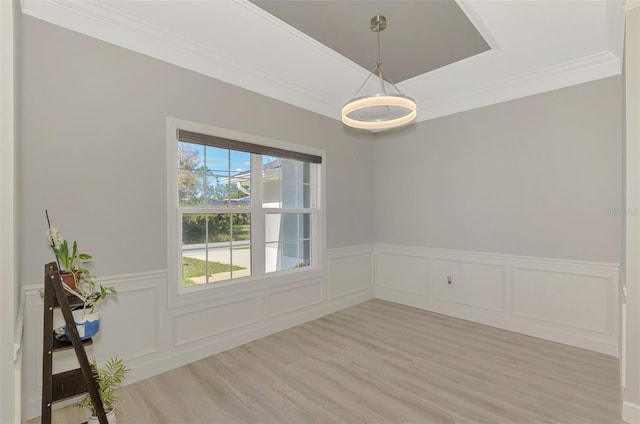 unfurnished dining area with a tray ceiling, ornamental molding, and light wood-type flooring