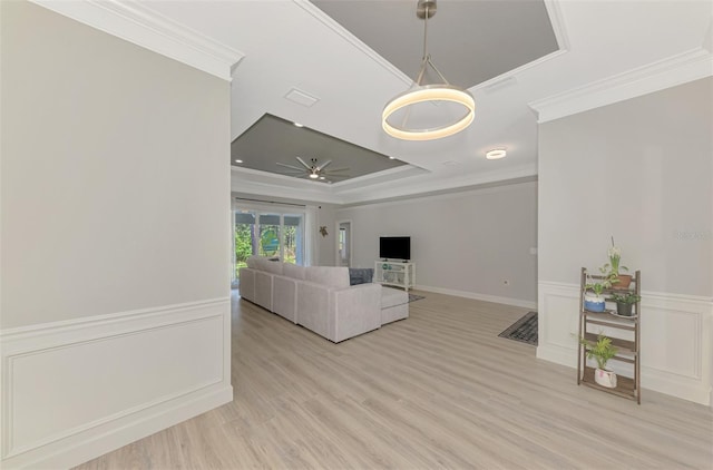 unfurnished living room featuring a raised ceiling, crown molding, light wood-type flooring, and ceiling fan