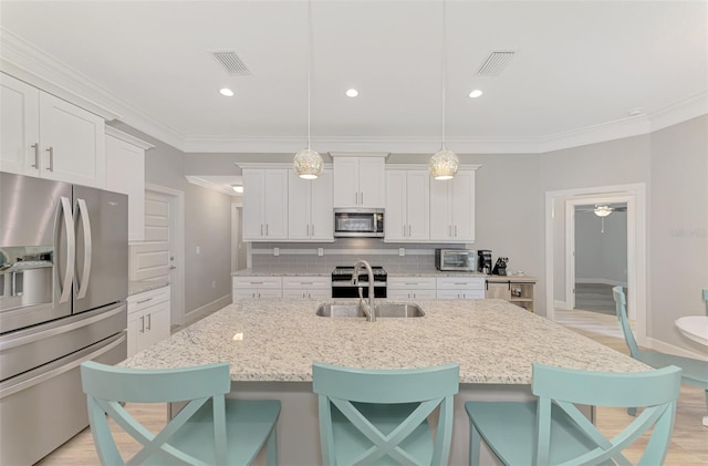 kitchen featuring white cabinetry, appliances with stainless steel finishes, hanging light fixtures, and a center island with sink