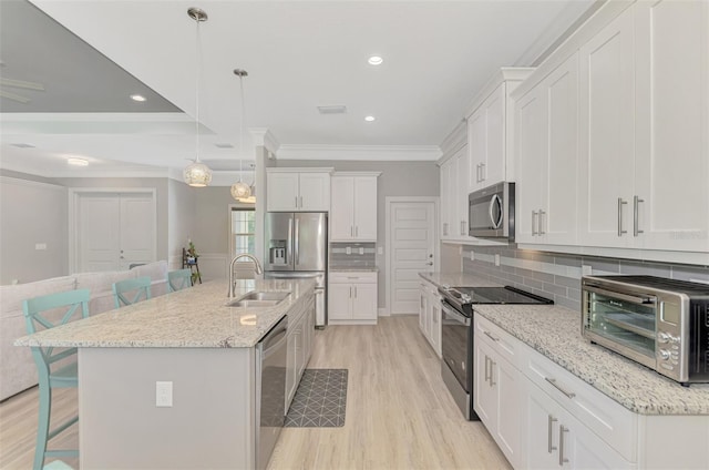 kitchen featuring appliances with stainless steel finishes, decorative light fixtures, sink, white cabinets, and a kitchen island with sink