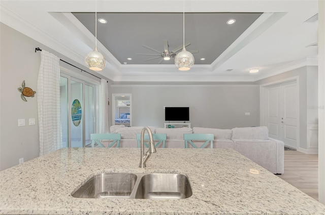 kitchen with hanging light fixtures, sink, light stone countertops, and a raised ceiling