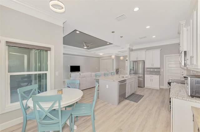 kitchen with sink, a kitchen island with sink, stainless steel appliances, white cabinets, and decorative light fixtures