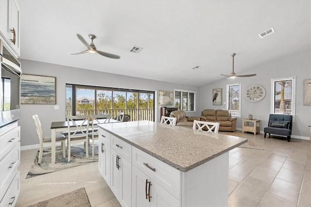 kitchen with light stone countertops, visible vents, white cabinets, and open floor plan