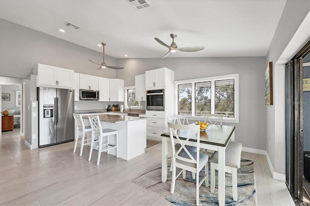 kitchen with a wealth of natural light, visible vents, appliances with stainless steel finishes, white cabinets, and a kitchen island