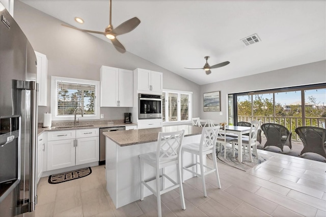 kitchen featuring dark stone counters, a center island, stainless steel appliances, white cabinetry, and a sink