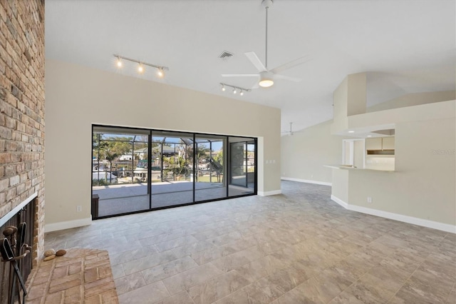 unfurnished living room with ceiling fan, track lighting, high vaulted ceiling, and a brick fireplace