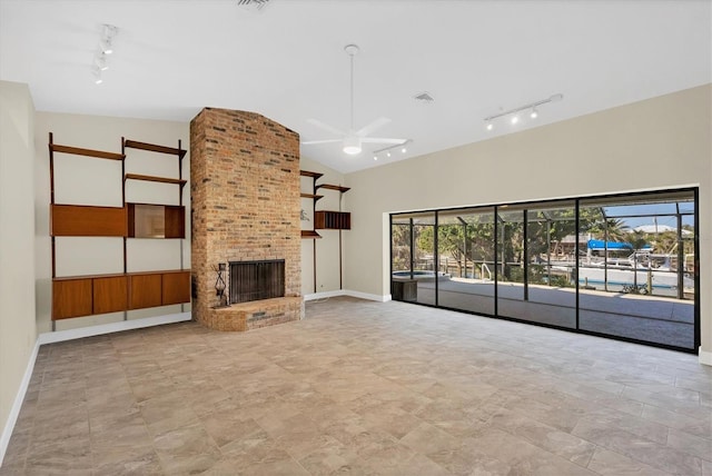 unfurnished living room with vaulted ceiling, rail lighting, ceiling fan, and a fireplace