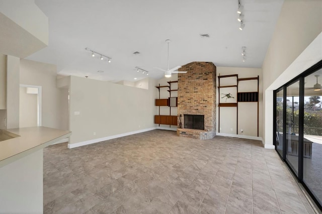 unfurnished living room with lofted ceiling, a brick fireplace, and track lighting