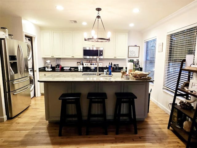 kitchen with appliances with stainless steel finishes, decorative light fixtures, white cabinetry, stacked washer / drying machine, and light stone countertops