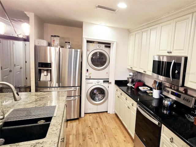 kitchen with sink, appliances with stainless steel finishes, stacked washer and clothes dryer, light stone counters, and light hardwood / wood-style floors