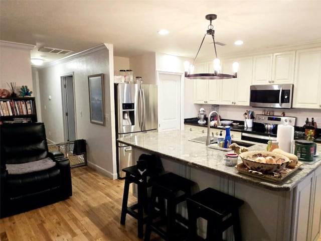 kitchen with sink, light stone counters, appliances with stainless steel finishes, pendant lighting, and white cabinets