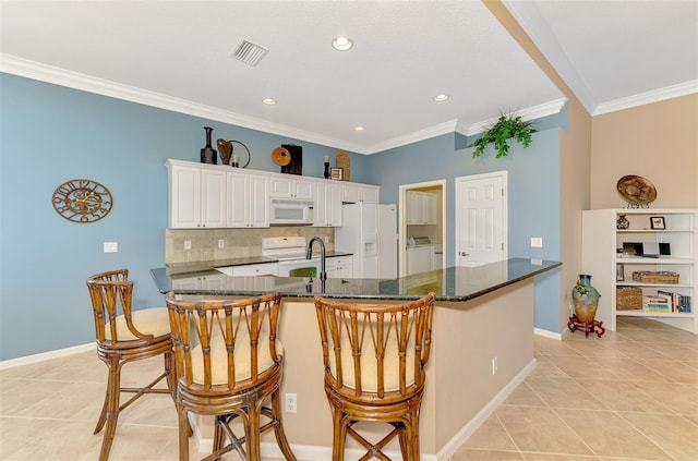 kitchen featuring white cabinetry, dark stone countertops, a kitchen bar, washing machine and dryer, and white appliances