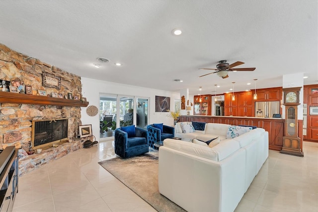 tiled living room featuring ceiling fan, a stone fireplace, and a textured ceiling