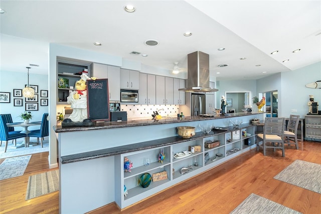 kitchen featuring pendant lighting, appliances with stainless steel finishes, island range hood, kitchen peninsula, and light wood-type flooring