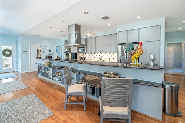 kitchen with tasteful backsplash, light hardwood / wood-style flooring, appliances with stainless steel finishes, kitchen peninsula, and island exhaust hood