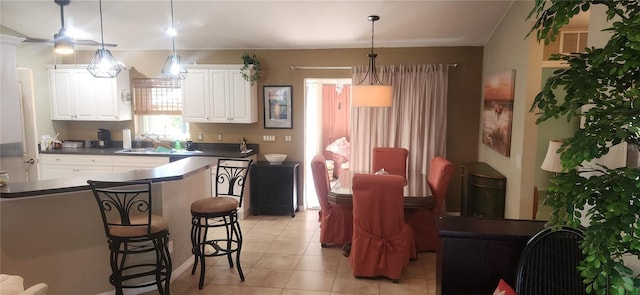 kitchen featuring a kitchen breakfast bar, white cabinets, pendant lighting, light tile patterned floors, and sink