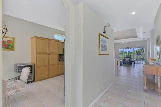 corridor with beverage cooler, a tray ceiling, and light tile patterned floors