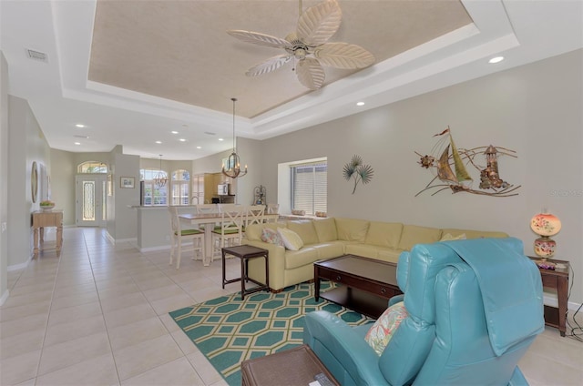 living room featuring a tray ceiling, ceiling fan with notable chandelier, and light tile patterned floors